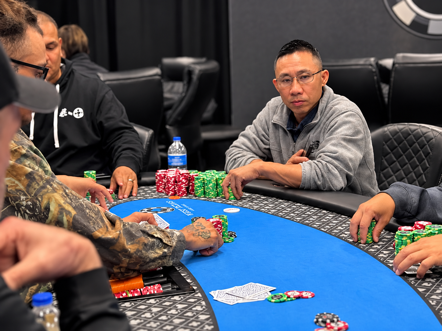 Players gathered around a blue-felt poker table with cards and stacks of chips